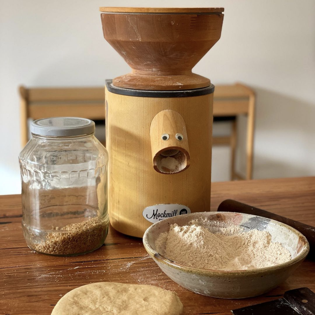 Mockmill 200 PRO Professional MOCK wooden grain, flour, pulses, legumes and spice fresh in home mill for personal use on wooden bench with a jar of brown rice and a bowl of freshly ground rice flour and dough