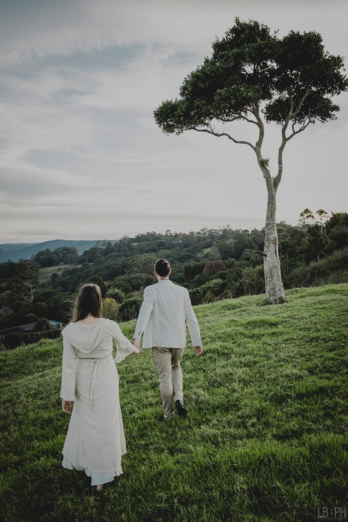 Eden Tree Eco Co-Creators Dan & Candice Kennedy walk hand in hand towards tree at One Tree Hill, Maleny, Queensland. Photo by Lauren Biggs Photography.