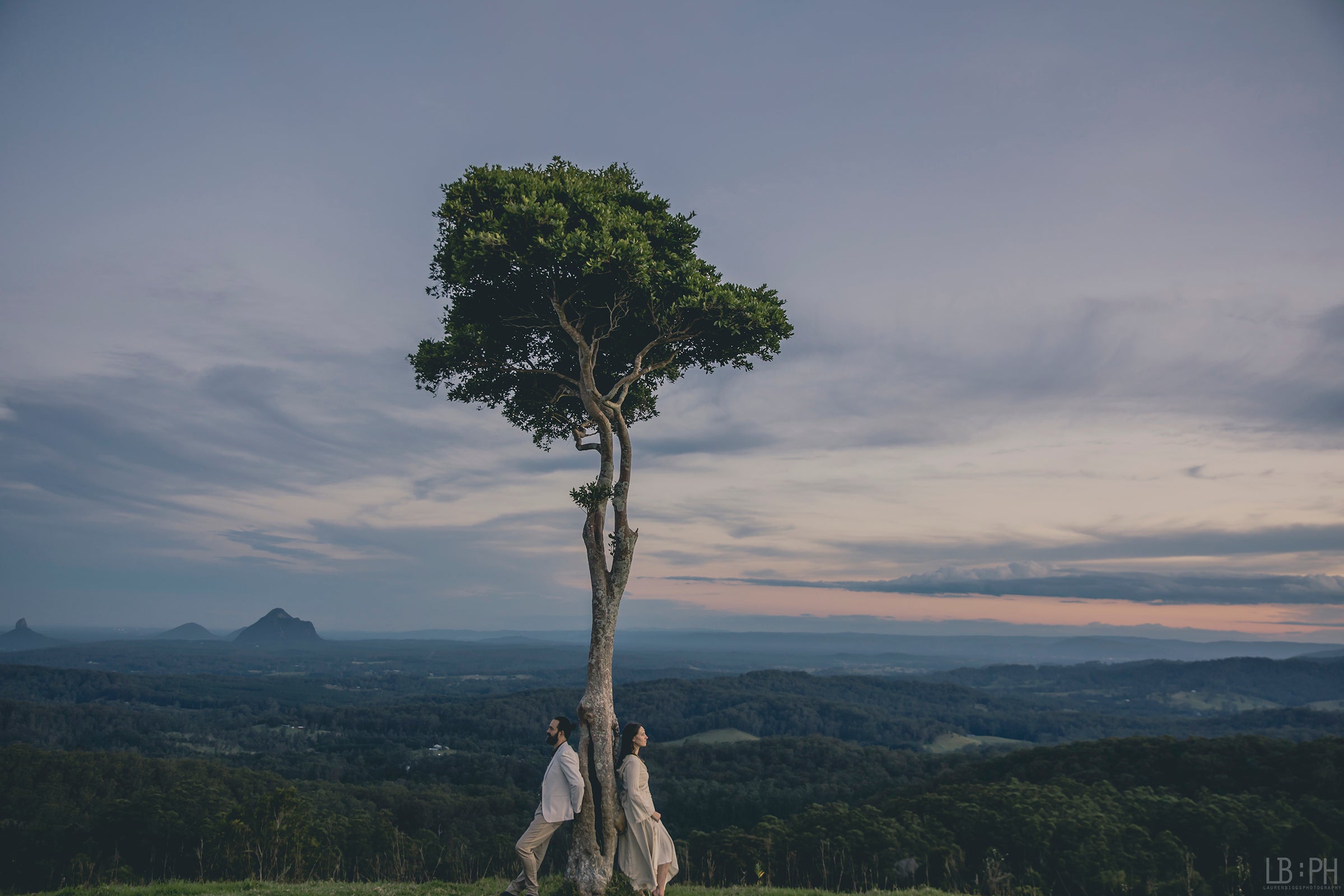 Eden Tree Eco; Co-Creators Dan and Candice Kennedy standing back-to-back against an Eden Tree overlooking the Glass House Mountains at sunset.