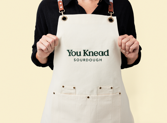 Person in a black shift wearing the You Knead Sourdough Chef Bakers Apron on a cream background