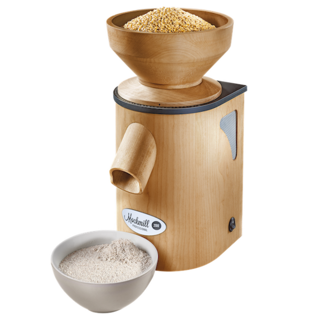 The Mockmill 200 PRO professional MOCK wood appliance with wheat grains in the hopper / top and a white bowl of freshly milled ground flour