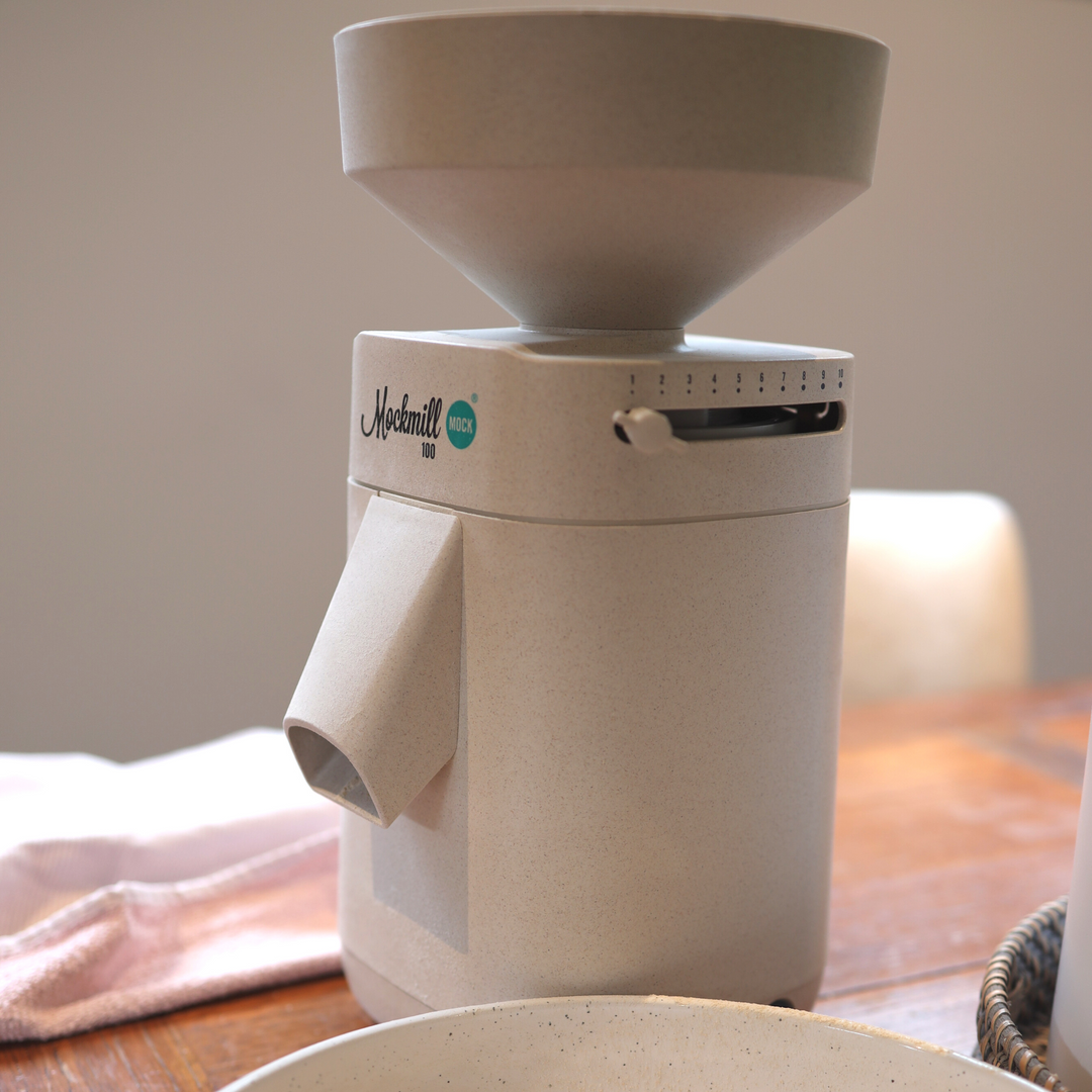 A Mockmill 100 MOCK appliance sitting on a wooden kitchen bench next to a tea towel and bowl